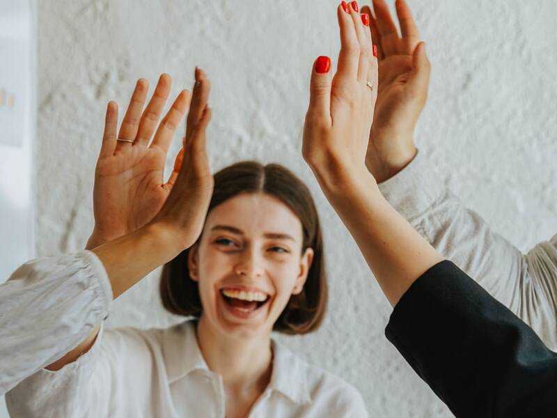Eine lachende Frau mit schulterlangen Haaren, die sich mit drei anderen Kollegen, deren Hände man nur sieht ein High Five gibt.